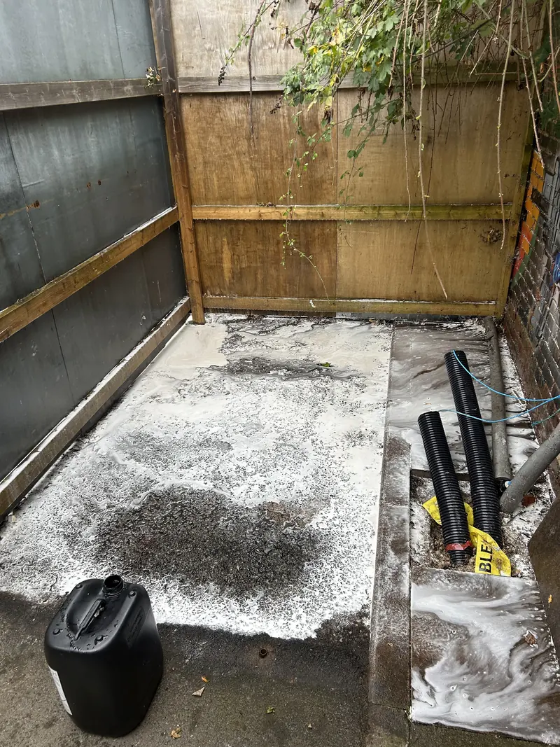 Concrete bin store floor being treated, with cleaning equipment by the fence