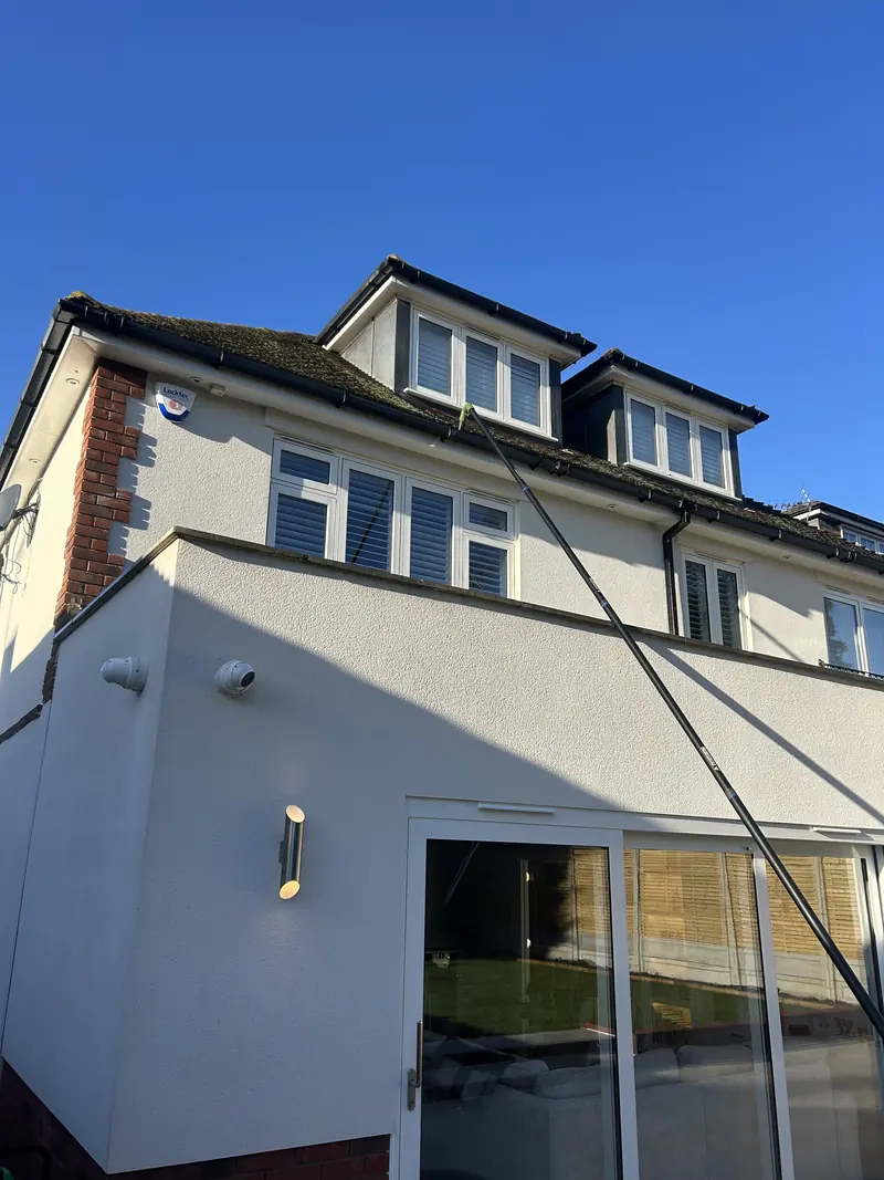 Gutter vacuum pole raised to the roofline of a white rendered house