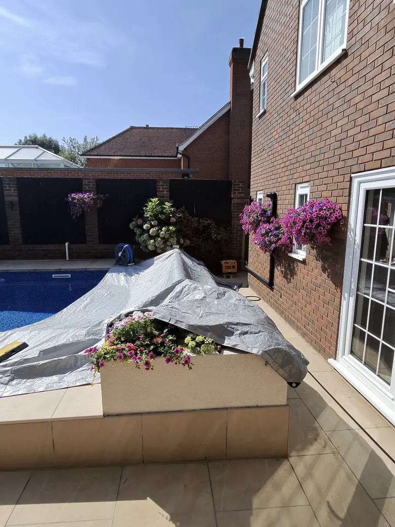 Patio beside a pool with a covered pool and flower baskets on the wall