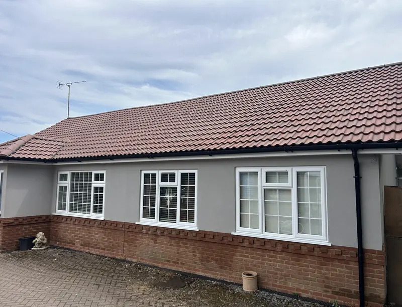 Grey rendered bungalow with a red tiled roof and white windows