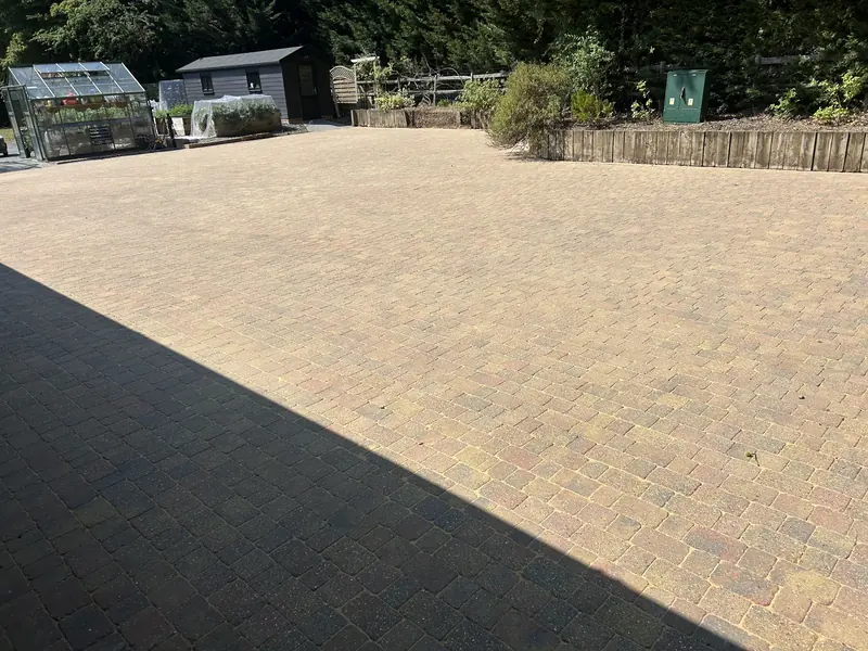 Large block-paved yard after cleaning, with greenhouses behind