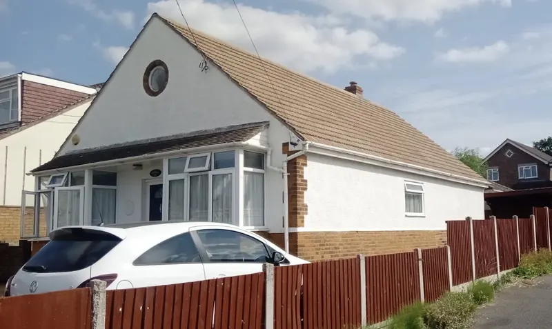 White bungalow with a tiled roof behind a wooden fence