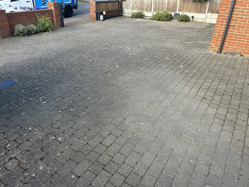Grey block-paved driveway before cleaning, with dark staining